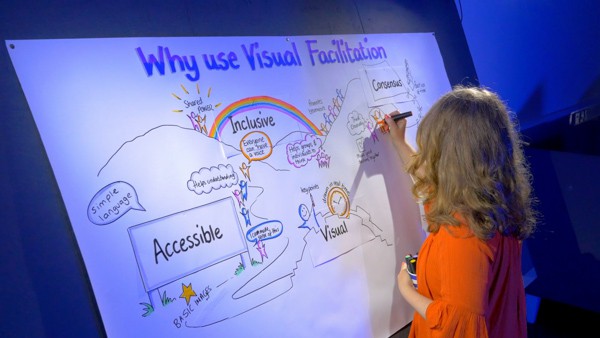 A woman draws colourful text and graphics on a large piece of papaer.